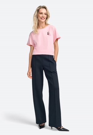 Maglietta corta rosa con maniche corte e grafica di cuffie, abbinata a pantaloni neri a vita alta e décolleté nere a punta.