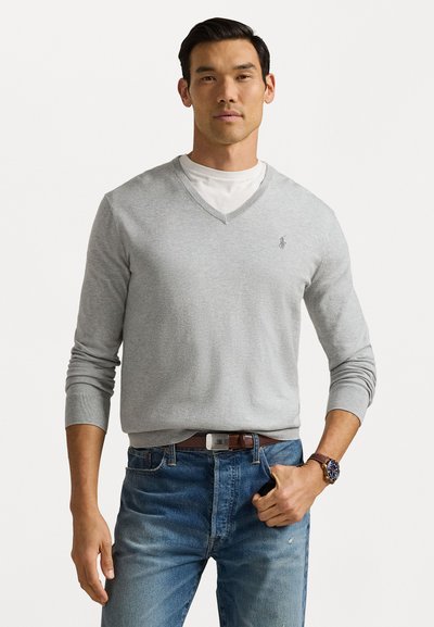 Grå v-hals sweater lavet af blødt strikstof, med ribbede manchetter og et lille logo på brystet, parret med blå jeans og et brunt bælte.