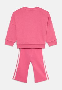 Ensemble en coton rose comprenant un sweatshirt et un pantalon court. Le sweatshirt a des épaules tombantes ; le pantalon présente des bandes latérales blanches et une coupe décontractée.