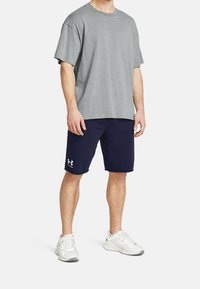 Grå kortärmad t-shirt, marinblå shorts med vit logotyp och ljusgrå träningsskor. Tyget verkar mjukt; designen är avslappnad och luftig.