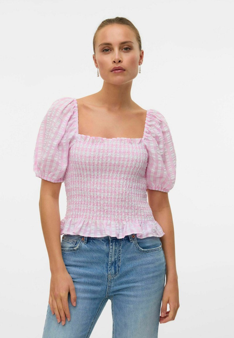 Sammenkrøpet rosa og hvitstripet topp med pufferm, firkantet utringning og volangkant. Kombinert med lyseblå jeans.