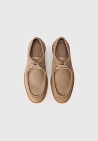 Rudi zomšos batai su apvalia nosimi, siuvinėjimu aplink kraštus ir lanksčiu guminio pado. Šnarančios juostelės yra surištos priekyje.