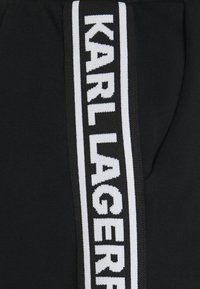 Czarna tkanina z szaro-białym paskiem bocznym, featuring napis "KARL LAGERFELD" w wyraźnym, pogrubionym tekście. Gładka faktura.