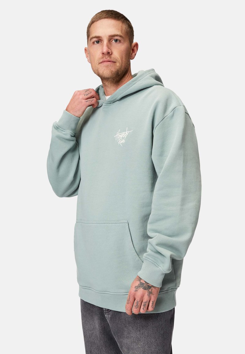 Ljusgrön hoodie i mjukt material, med en framficka, ribbade ärmslut och en logotyp på bröstet. Slät yta och oversized passform.