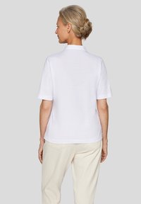 Weißes Poloshirt mit kurzen Ärmeln, gerader Schnitt und weicher Textur, mit einem klassischen Kragen und einem schlichten Rückendesign.