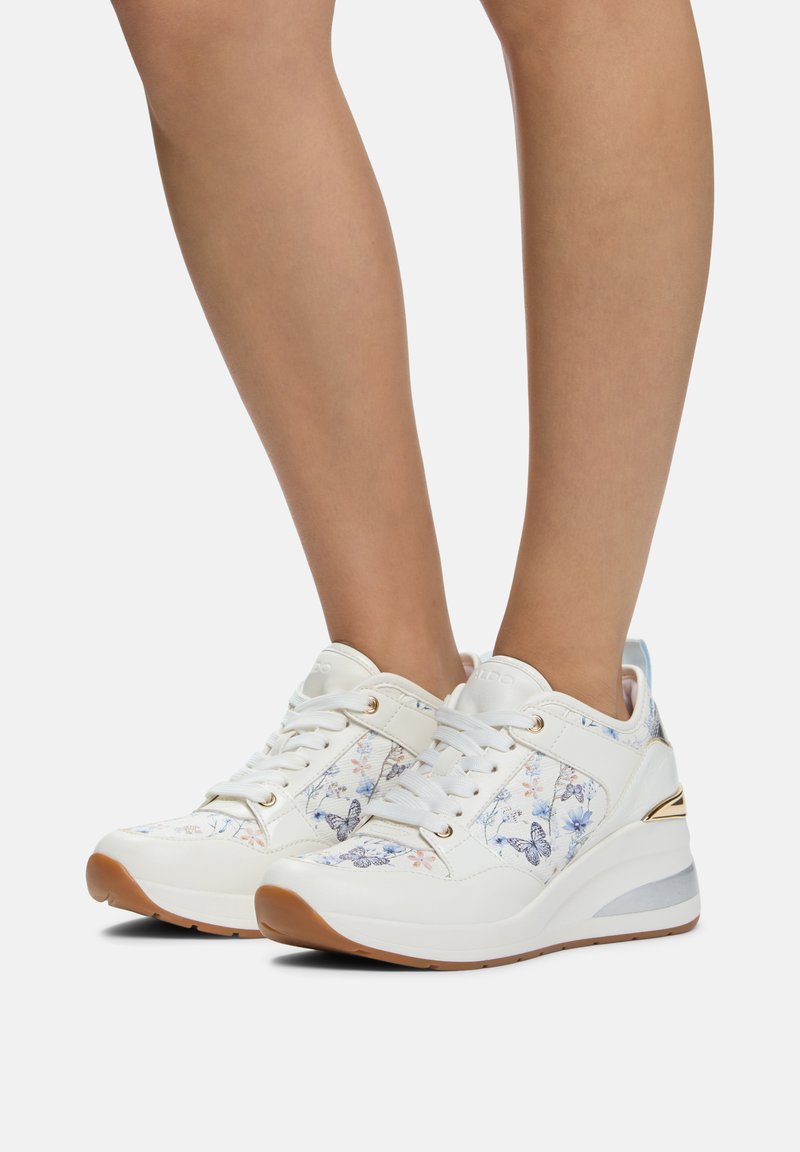 Białe sneakersy z kwiecistym wzorem w odcieniach niebieskiego i różowego, z amortyzującą podeszwą, sznurowanym przodem i lekko podwyższonym obcasem.