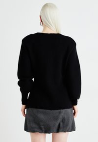 Black knitted sweater with wide sleeves, textured fabric, and a crew neckline, paired with a pinstriped skirt.