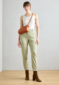 Pantalones cargo de tejido verde claro con bolsillos laterales, combinados con una camiseta sin mangas blanca y botines de ante marrón de tacón. Lleva un bolso marrón.