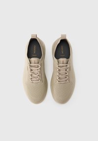 Μπεζ αεριζόμενα αθλητικά παπούτσια με υφή στην επάνω επιφάνεια, σχέδιο με κορδόνια και μαξιλαρωμένη γλώσσα. Διαθέτουν λεία καουτσούκ σόλα και ελάχιστη σήμανση.