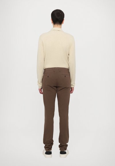 Polo shirt bej cu mânecă lungă alăturat cu pantaloni căprui, cu un design ajustat, textură netedă și detalii subtile ale buzunelului din spate.