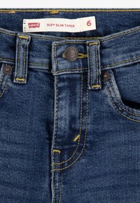 Levi's 512 Slim Taper -farkut, tummansinistä denimkangasta, jossa keltaiset saumat, metallinen nappi ja viiden taskun malli. Kokoetiketti näkyvissä.