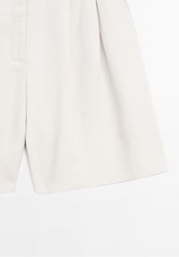 Pantalon large beige à plis sur le devant, en tissu lisse, présenté sur un fond blanc.