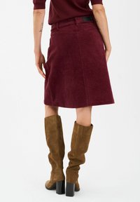 Bordowa spódnica z korduroy z detalami teksturalnymi, do kolan, z czarną metką w talii, w połączeniu z brązowymi zamszowymi kozakami za kolano.