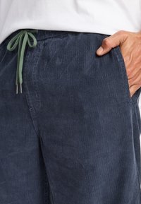 Navy corduroy pants with vertical stripes, featuring a drawstring waistband in green and side pockets. Texture appears soft and ribbed.