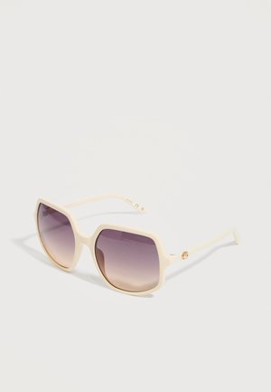 Lunettes de soleil carrées surdimensionnées de couleur crème avec des verres dégradés violets et des branches fines sur une surface blanche.