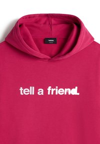 Haut à capuche fuchsia avec une grande impression de texte blanc "parle à un ami" sur le devant. Dispose d'un capuchon avec cordon et d'un tissu doux et texturé.