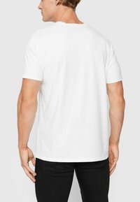 T-shirt bianco in cotone con maniche corte e colletto tondo, caratterizzato da un orlo dritto e una superficie liscia. Visualizzato dalla parte posteriore.