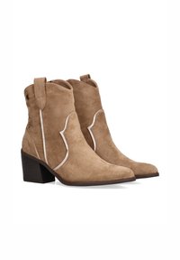 Botines de ante beige con punta afilada, costuras de acento blancas y un tacón apilado. Presentan lengüetas laterales para facilitar su uso.