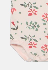 Blomstrete bodysuit med myk kremfarget stoff og røde og grønne blomster mønstre, avsluttet med trykknapper nederst.