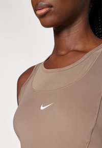 Canotta atletica marrone con scollatura rotonda e piccolo logo Nike bianco. Tessuto liscio con un design aderente che evidenzia le curve del corpo.