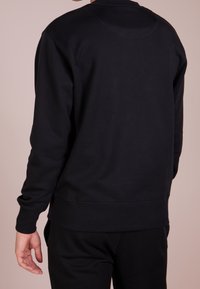 Sudadera de algodón negra con escote redondo, puños acanalados y dobladillo. Textura suave, diseño minimalista y sin logotipos ni patrones visibles.