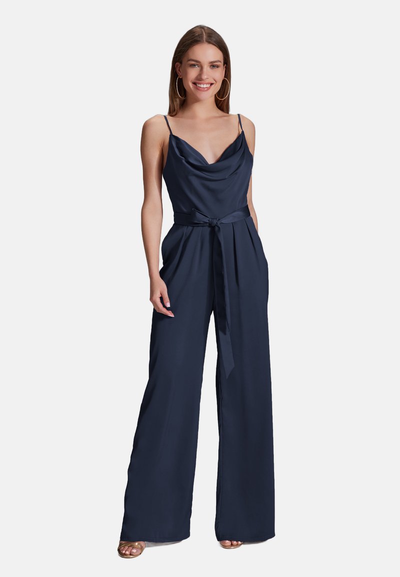Combinaison en satin bleu marine avec un décolleté drapé, des bretelles fines, une ceinture nouée à la taille et une coupe large, dotée de poches latérales et d'une texture lisse.