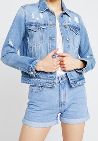 Ljusblå denimjacka med slitna detaljer, knapstängning och två bröstfickor. Matchad med ljusblå shorts med uppvikt fåll.