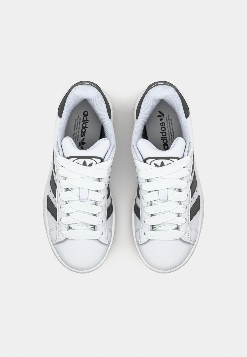 Zapatillas deportivas blancas con rayas negras, diseño de cordones, cuello acolchado, textura de cuero suave y logotipo en la lengüeta.