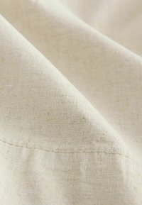 Linen tkanina prirodne boje s glatkom teksturom, vidljivim uzorkom tkanja i suptilnim sjajem. Tkanina je naborana, pokazujući nježne nabore.