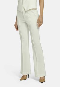 White tailored pants with flared legs, featuring precise stitching and a smooth texture. Worn with beige pointed-toe heels.