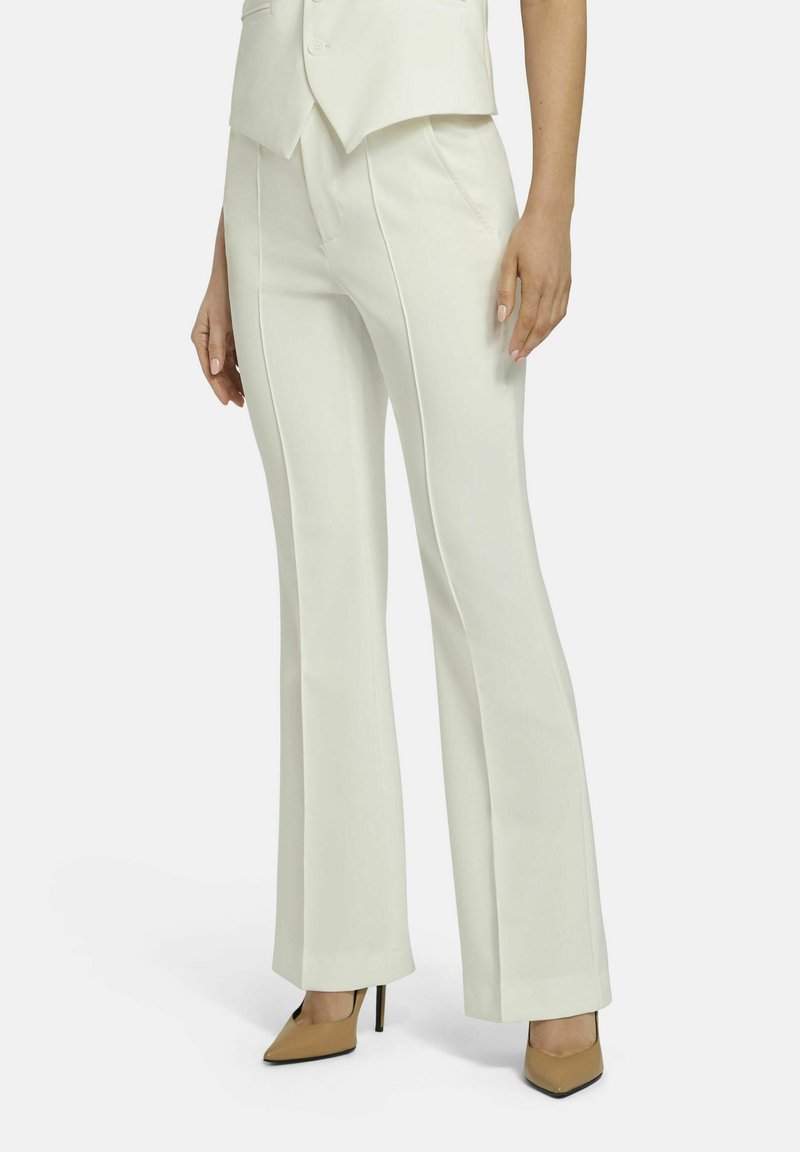 White tailored pants with flared legs, featuring precise stitching and a smooth texture. Worn with beige pointed-toe heels.
