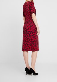 Punainen mekko, jossa on musta leopardikuvio, lyhyet hihat, polvipituinen, valmistettu sileästä kankaasta, yhdistetty mustiin korkokengiin.