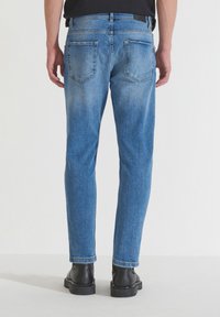 Jeans de mezclilla azul con un corte recto, que presentan dos bolsillos traseros, un ligero desgaste y dobladillos deshilachados, combinados con botas negras.