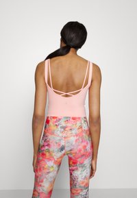 Top desportivo cor-de-rosa com um design de costas cruzadas, combinado com leggings coloridas com padrão floral e silhueta ajustada.