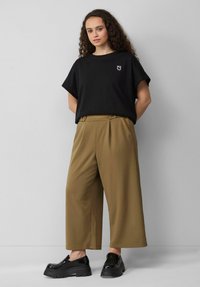 T-shirt noir surdimensionné avec un petit graphisme blanc, associé à un pantalon large taille haute en kaki et des chaussures noires imposantes.