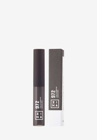Mascara à sourcils dans un tube marron foncé avec finition mate. Accompagné d'une boîte en carton rectangulaire arborant un texte noir audacieux sur fond blanc.