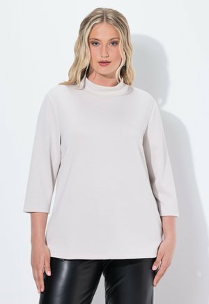 Lichtbeige coltrui met driekwartmouwen, gemaakt van een zachte stof. Heeft een relaxte pasvorm en een minimalistisch design, zonder patronen.