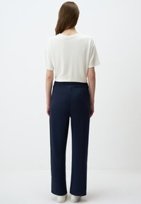 Casual outfit met een witte, korte mouwen shirt en zee blauwe, wijde broek. De broek heeft een elastische tailleband en een gladde textuur.
