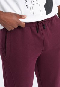 Burgunderfarbene Jogginghosen aus leichtem Stoff, mit elastischem Bund und Kordelzug sowie seitlichen Taschen für zusätzliche Funktionalität.