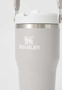 Stanley mug in light gray with a matte finish, white lid, stainless steel accent band, and logo featuring a bear with wings.