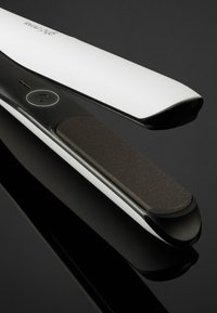 Witte en zwarte haardroger met getextureerde zwarte keramische platen en een aan/uit-knop op het handvat, geplaatst tegen een reflecterend zwart oppervlak.