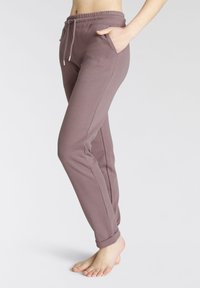 Lila Baumwoll-Jogginghosen mit elastischem Bund und Kordelzug. Sie verfügen über Seitentaschen und einen gerippten Saum. Subtile Markenkennzeichnung am Oberschenkel.