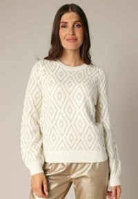 Pull en tricot blanc avec un motif en diamants de couleur vert clair, des poignets et un ourlet côtelés, et une coupe décontractée. Associé à un pantalon beige métallique.