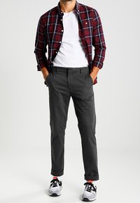 Rood en marineblauw geruit overhemd over een wit T-shirt, gecombineerd met grijze tapering chinos en zwart-witte sneakers.