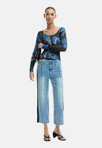 Must ja sinine pikkade varrukatega särk abstraktse mustriga; helesinised laiade säärega teksad külgse kontrastse paneeliga; mustad rihmikud sandaalid.