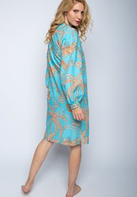 Blaues Blumenkleid mit Palm- und Lilienmustern, langen Ärmeln und lockerer Passform, aus leichtem Stoff mit glatter Textur.