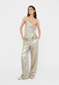 Top argintiu metalic fără mâneci, cu decolteu drapat, asortat cu pantaloni largi argintii metalici. Textură netedă, luciu subtil.