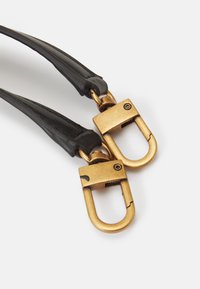 Des sangles en cuir noir avec des clips en métal doré ; les clips présentent un design courbé et un mécanisme de verrouillage pour un attachement sécurisé.