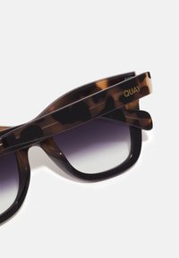 Gafas de sol de carey con lentes degradados, con acabado brillante. Logo "QUAY" grabado en la patilla. Forma cuadrada con bisagras resistentes.