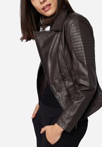 Braune Leder-Motorradjacke mit gesteppten Schulterakzenten, Reißverschluss-Taschen und taillierter Silhouette, getragen mit einem schwarzen Oberteil.